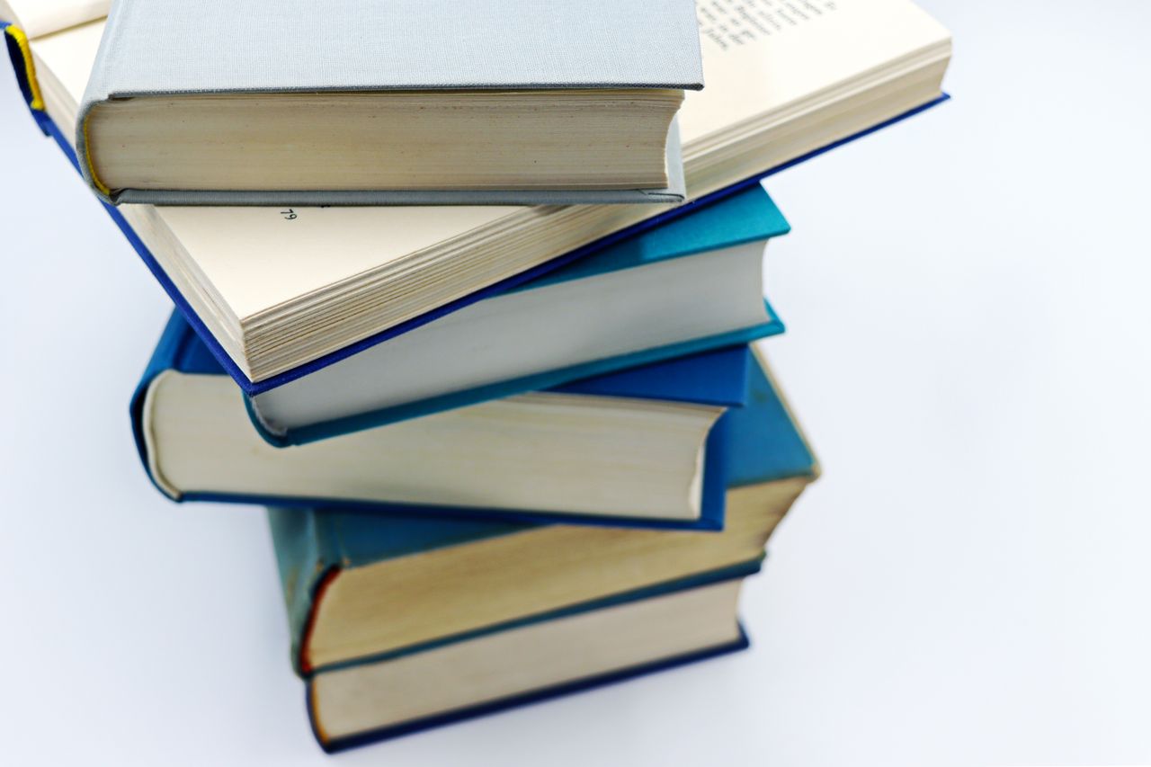 ours-journey A pile of books with blue covers on a white background, symbolizing education and knowledge.